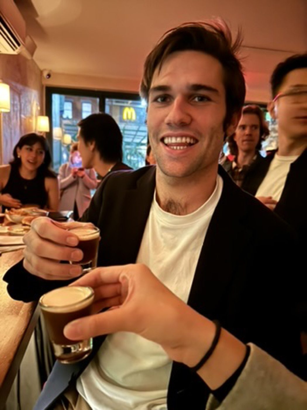 Smiling man holding two espresso drinks in a lively bar