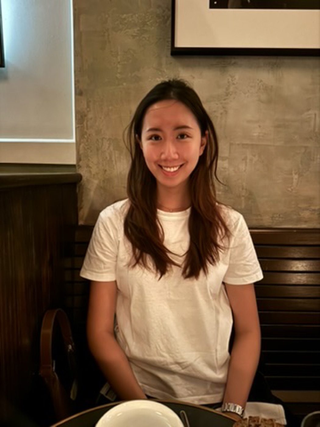 Smiling woman in a white tee at a warm-lit restaurant table