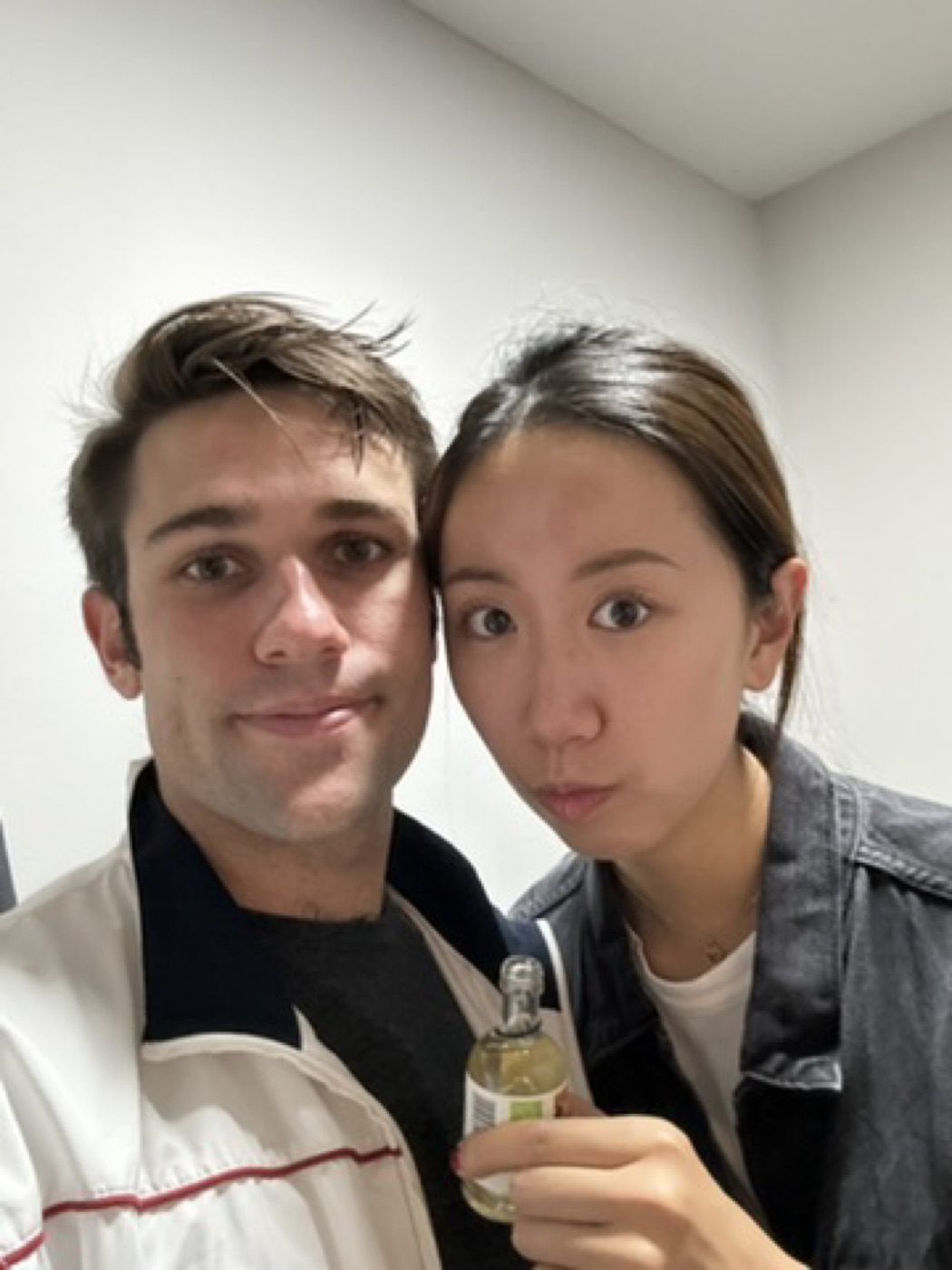 Couple selfie playfully holding up a small bottle of perfume