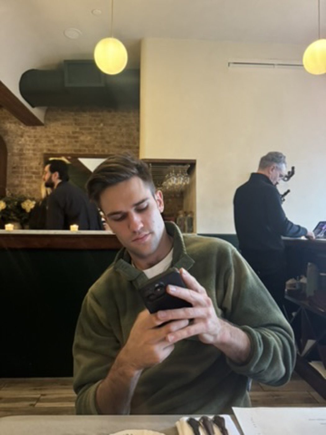 Man in green fleece reading his phone at a warm-lit cafe