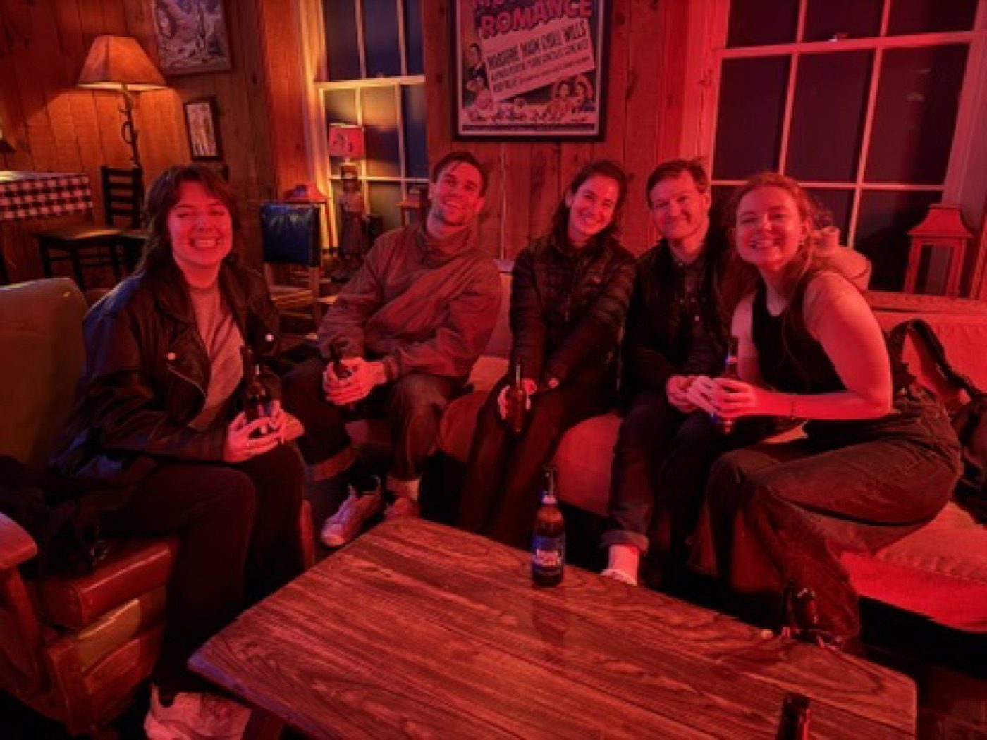Five friends cozy with beers in a red-lit lounge