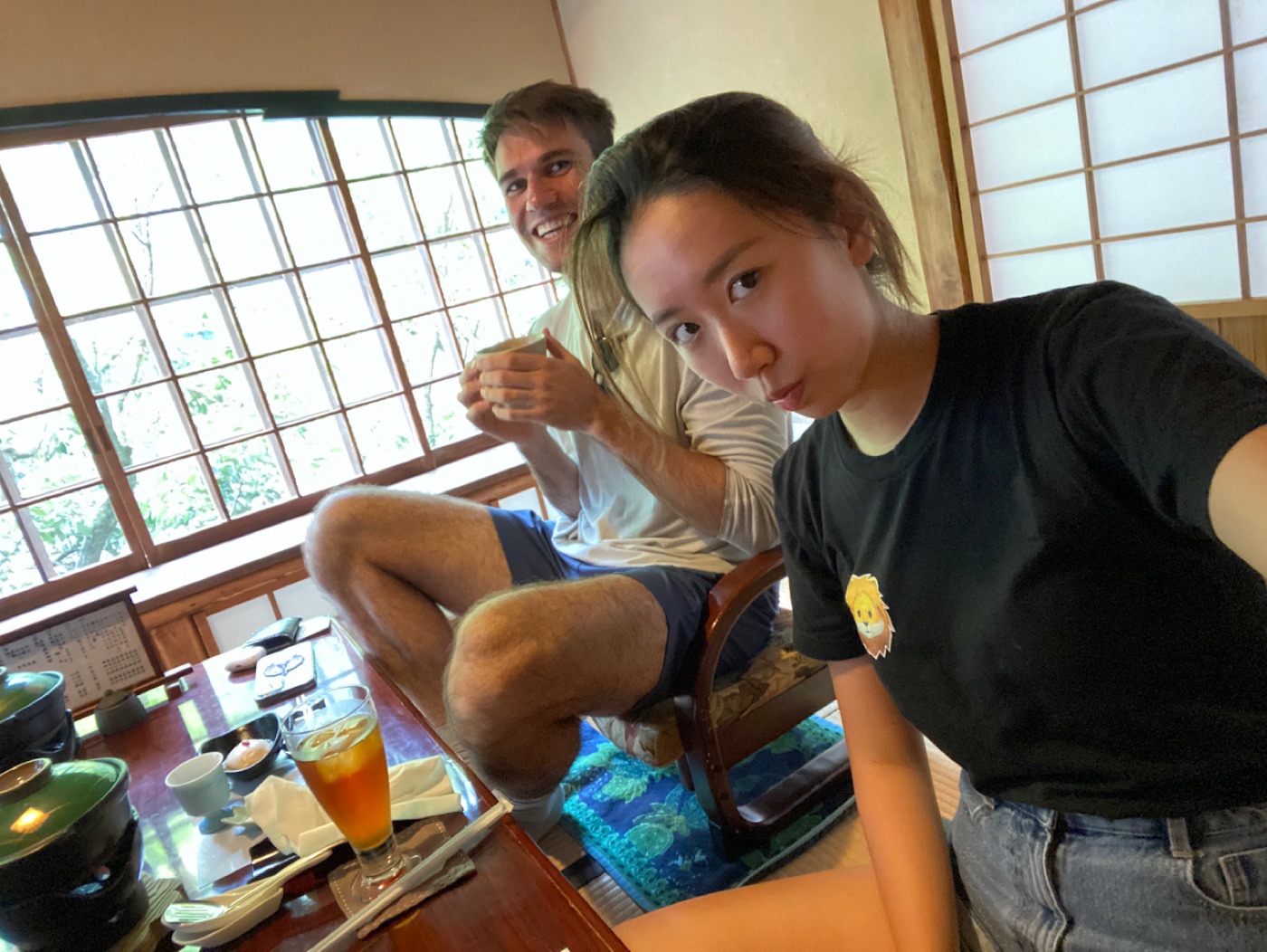 Tatami-room selfie: a woman pouts at the camera while Noel grins behind her with a teacup in hand.