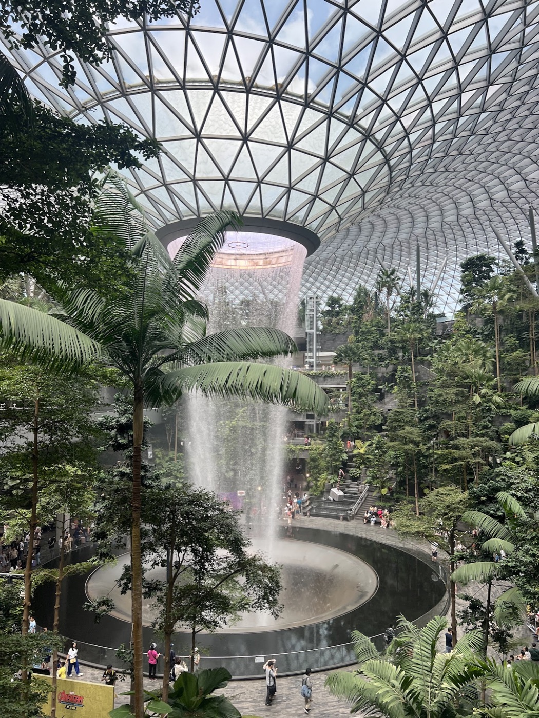 The Rain Vortex waterfall pours from the domed glass roof of Jewel Changi Airport into a rainforest-ringed pool.