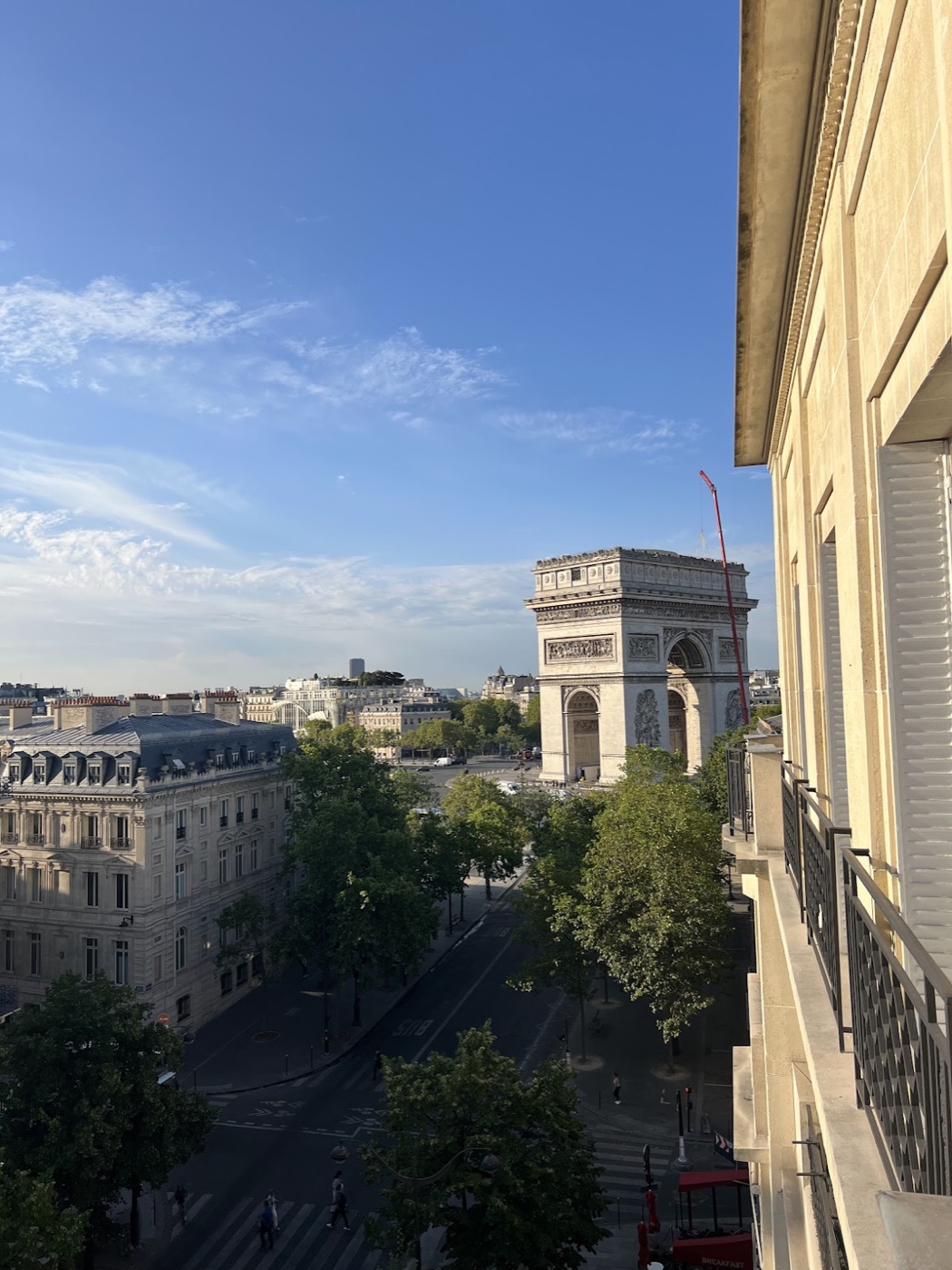 The Arc de Triomphe seen from a nearby balcony under a bright blue sky.