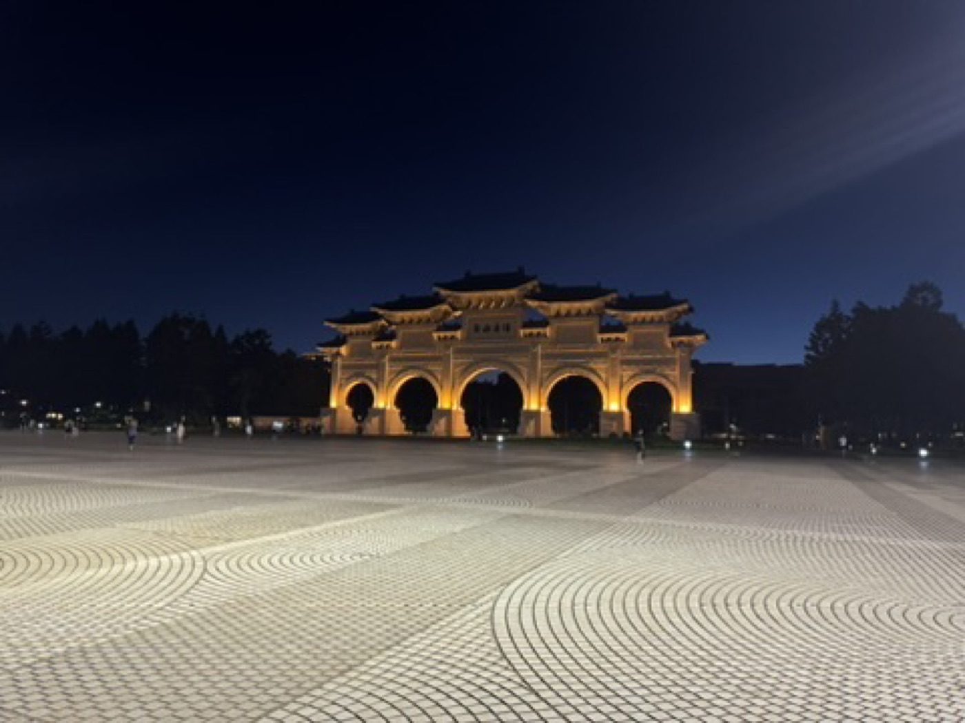 Illuminated Liberty Square gate at night over a patterned plaza
