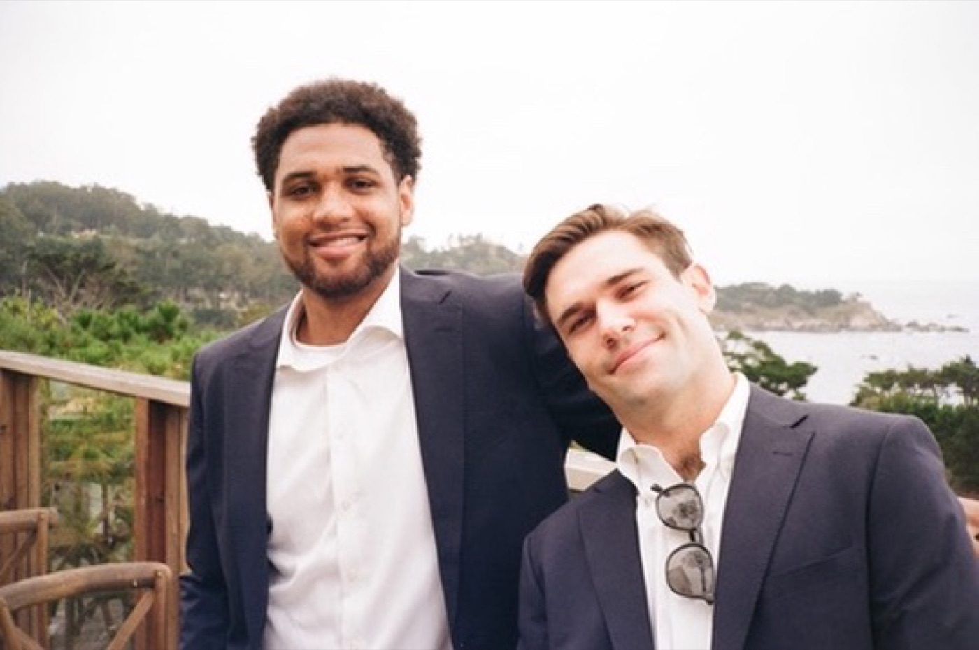 Two men in navy suits smiling above a rugged coastline