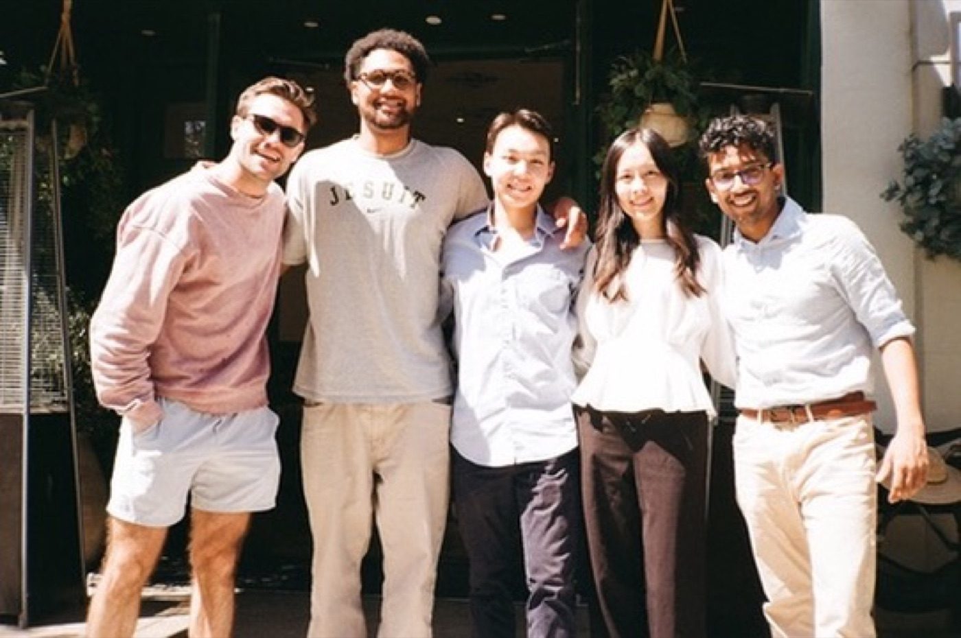 Five friends posing together outside a sunlit cafe