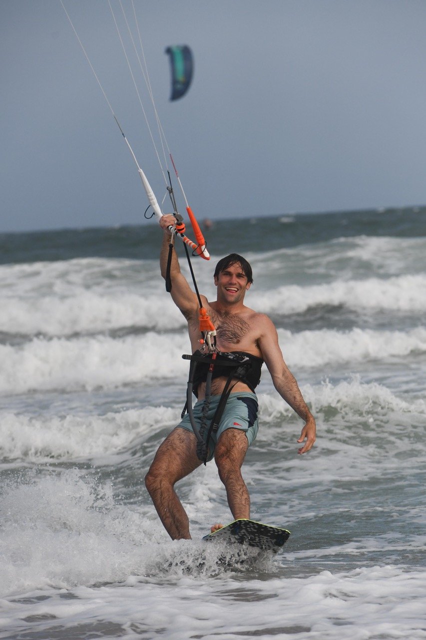 Riding in with a grin, kite up and a wave breaking behind