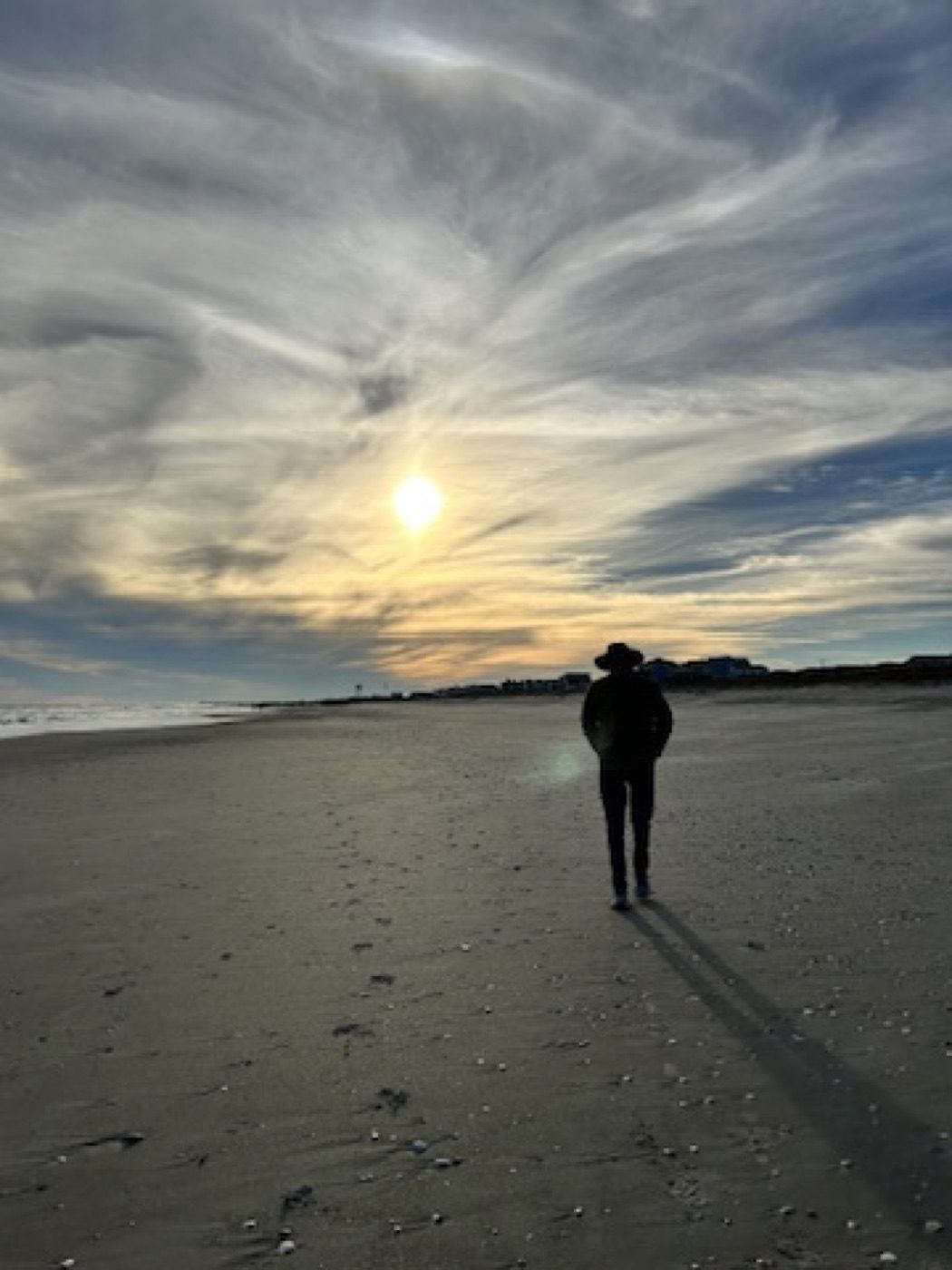 Lone silhouetted walker on the beach under dramatic sky