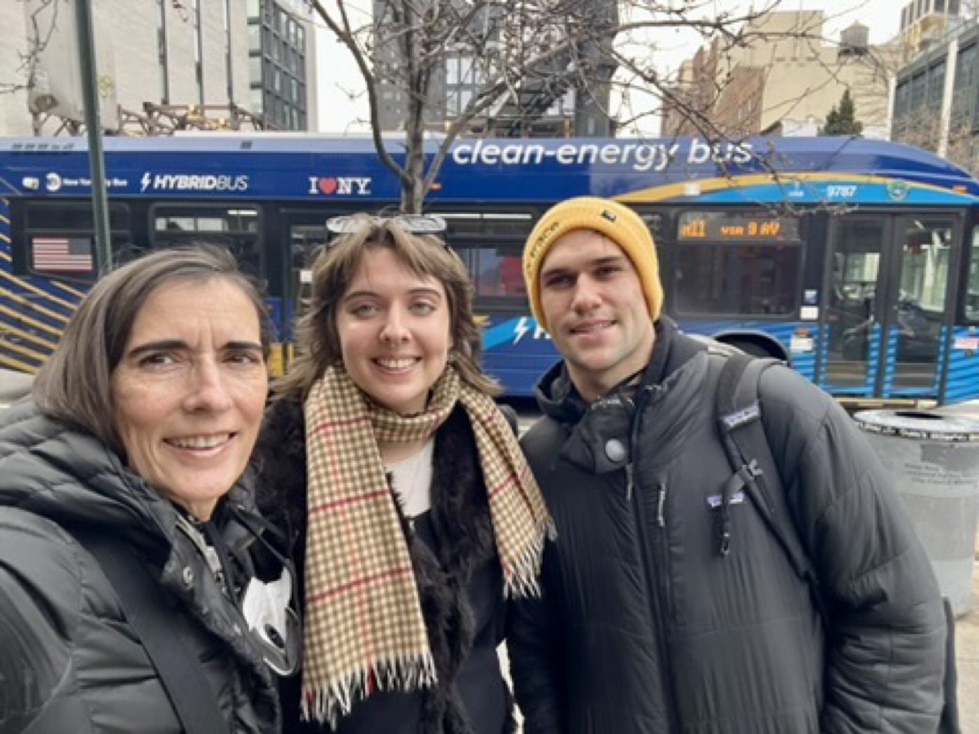 Three friends bundled up for a winter selfie by an NYC bus