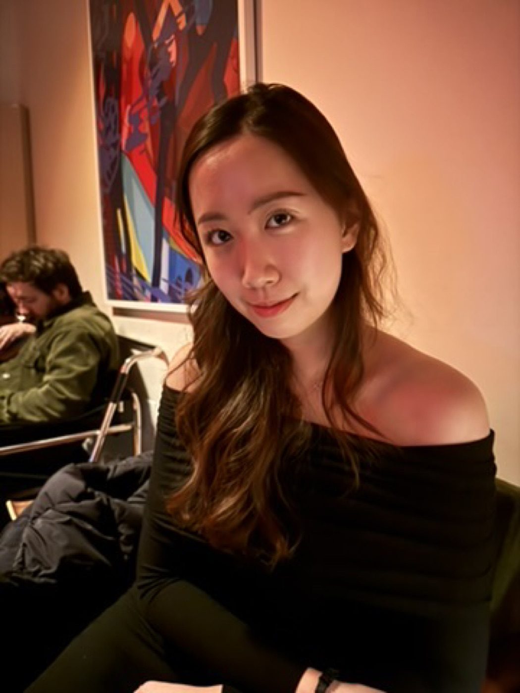 Warm-lit portrait of a woman in black, colorful art behind