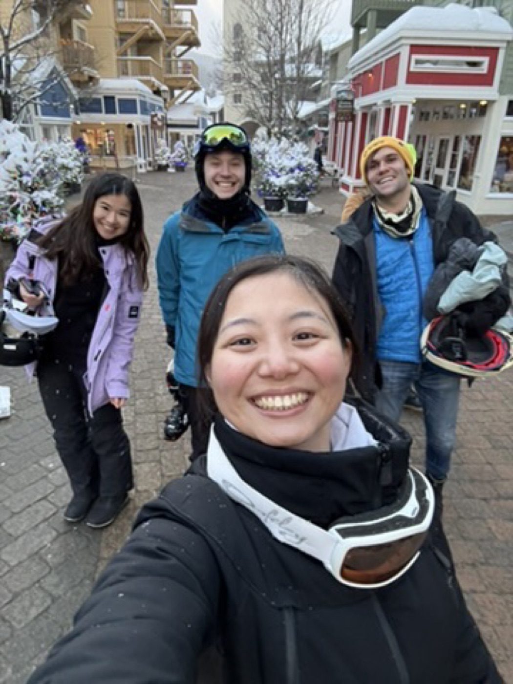 Four friends grinning on a snowy ski-village street