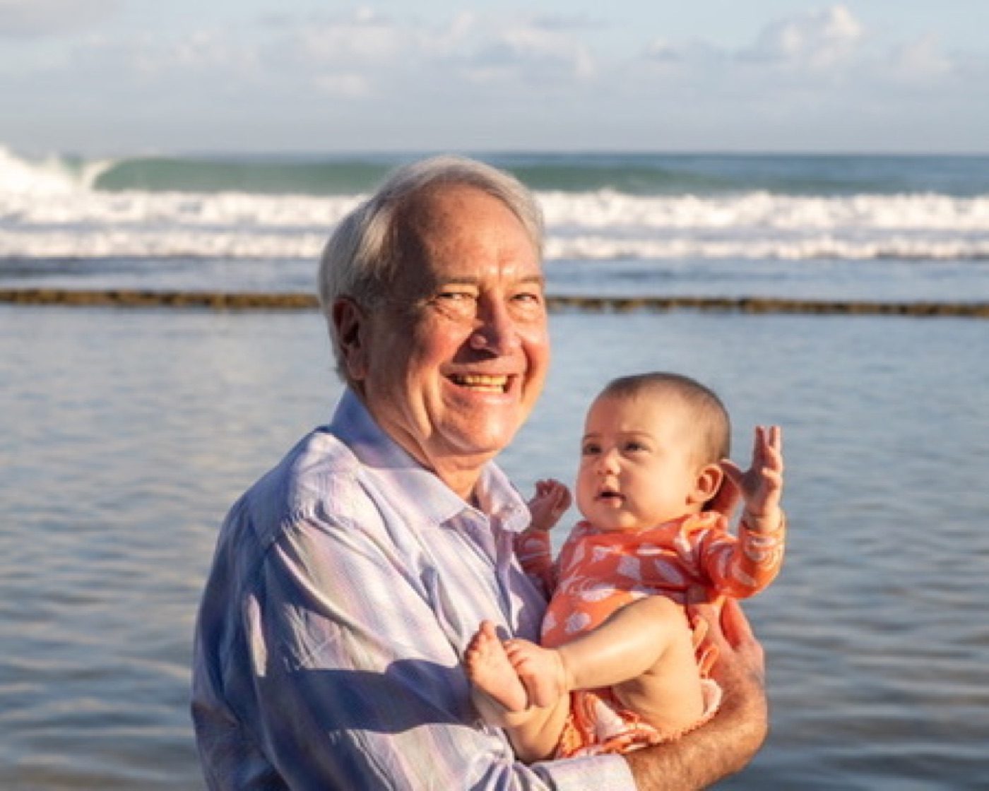 Grandfather laughing with a wide-eyed baby, waves behind
