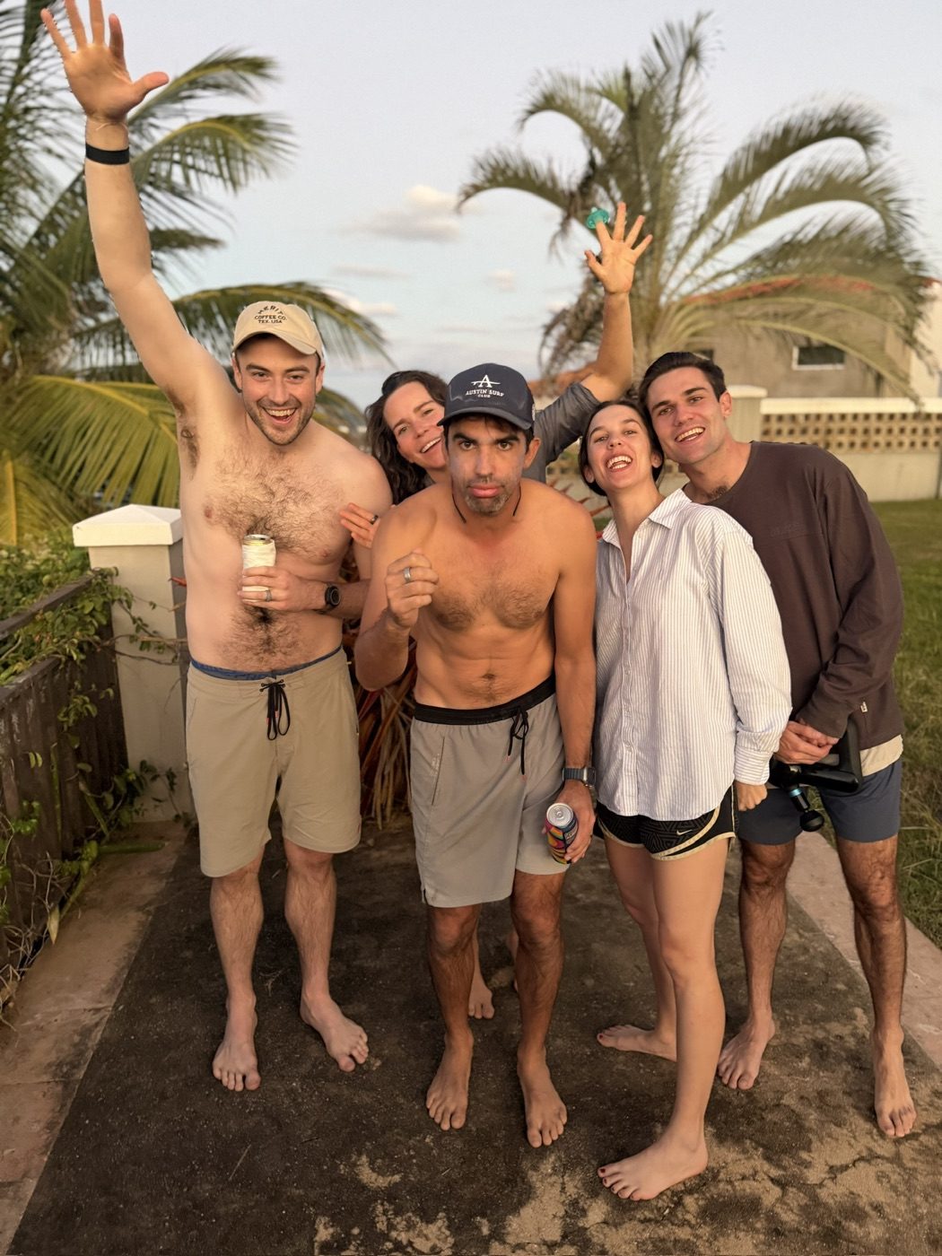 Five friends howling with laughter, hands up in the tropics