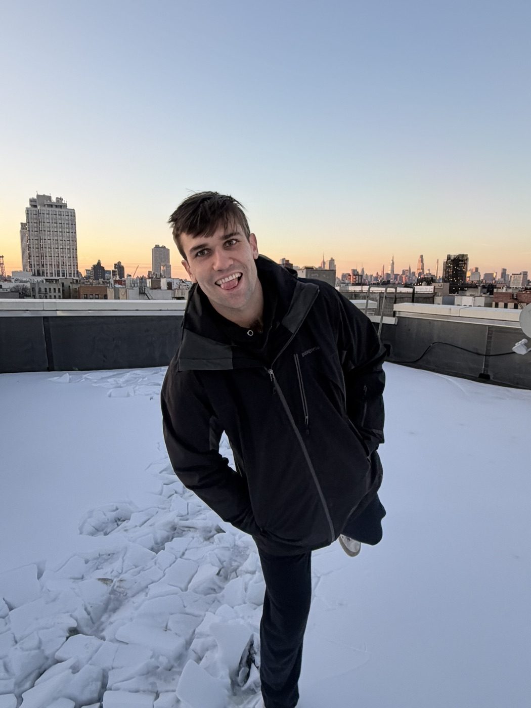 Goofy tongue-out grin on a snowy NYC rooftop at sunset